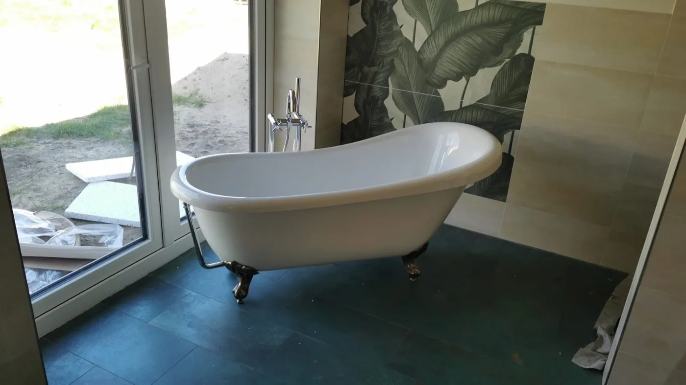 Freistehende weiße Badewanne auf dekorativen Füßen vor Wand mit Blattmotiv