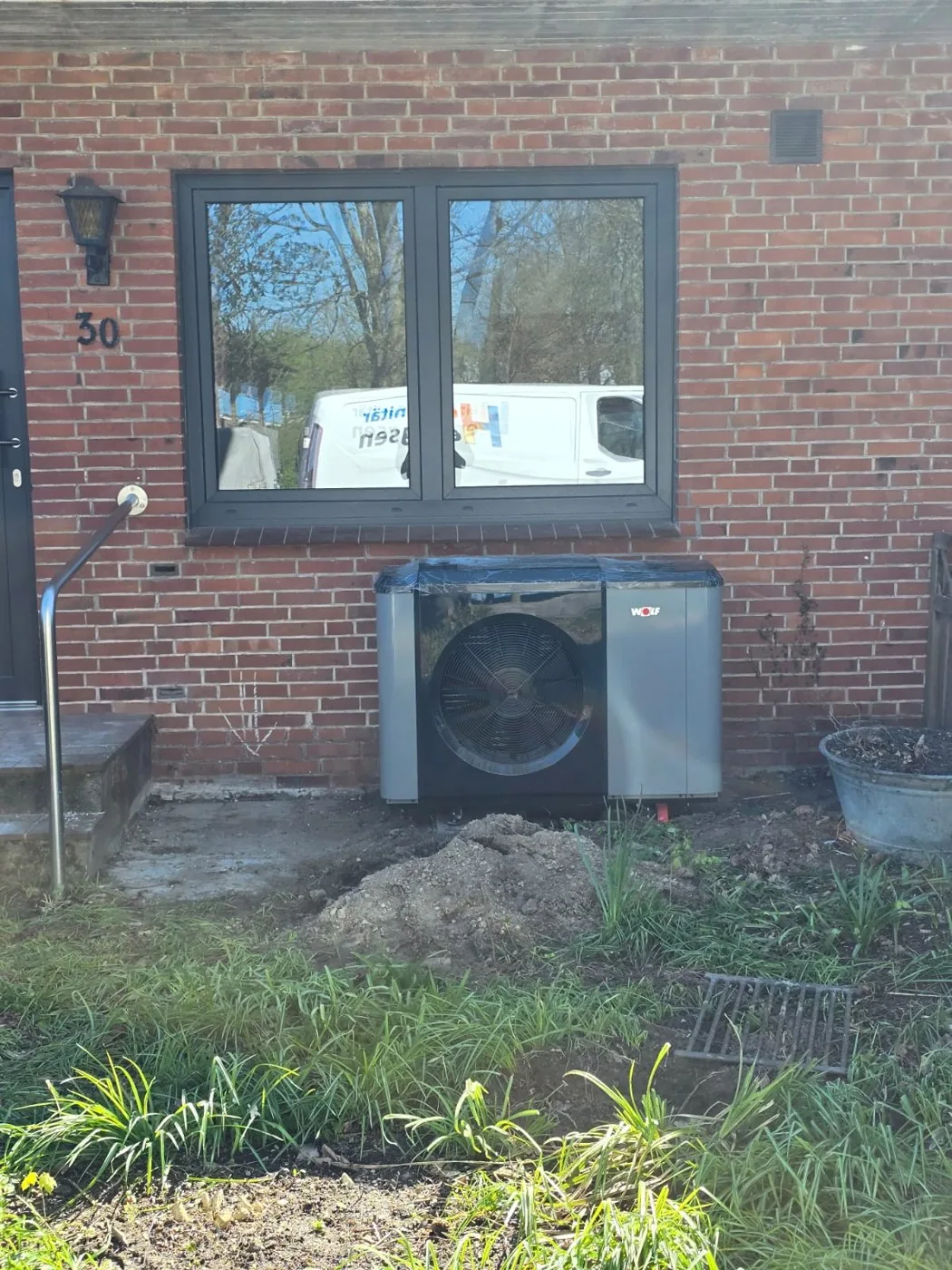 Außeneinheit einer Luft-Wasser-Wärmepumpe vor einer Klinkerfassade während der Bauarbeiten
